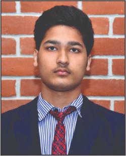 Portrait of a young man in a dark suit with a red tie, standing in front of a brick wall.