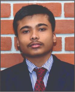Portrait of a young man in a dark suit with a striped shirt and red tie, posed against a brick wall.