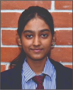 Portrait of a young student with dark hair, wearing a blue striped shirt, red tie, and blazer, in front of a brick wall.