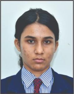 Portrait of a young woman in a school uniform looking at the camera; dark hair tied back, wearing a blue blazer, striped shirt, and red tie.