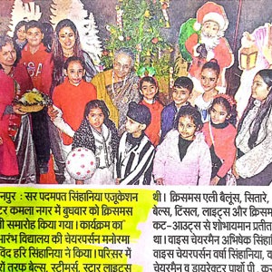 Group of children and adults posing with a Christmas tree and Santa Claus in the background.