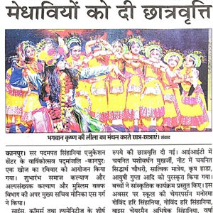 Group of young women in bright yellow traditional outfits performing a dance on stage during a cultural program; a performer in contrasting clothes stands at left.