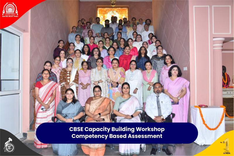 Group photo of workshop participants posing on a staircase for the CBSE Capacity Building Workshop banner in the foreground reading 'Competency Based Assessment' in a blue rounded plaque.