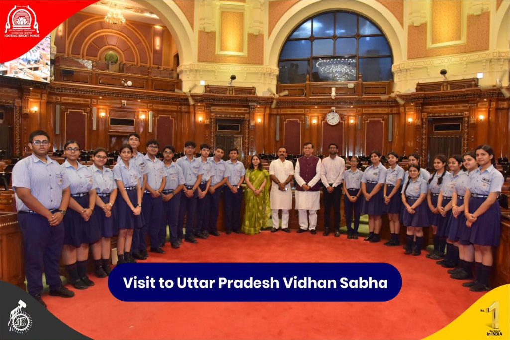 Group of students in blue uniforms posing with officials inside a grand legislative chamber during a Visit to Uttar Pradesh Vidhan Sabha poster event.