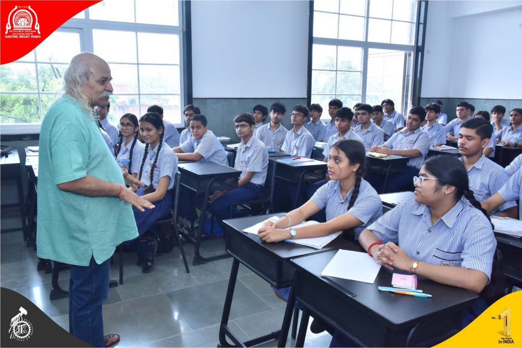 Inspiring Scientific Thinking Science Workshop with Padma Shri Prof H C Verma Older man with long white hair lecturing to attentive students in striped uniforms in a bright classroom. (Informative: teacher addressing class)