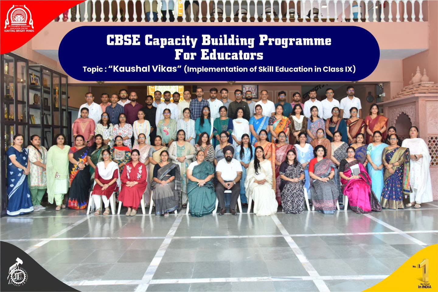 Group photo of teachers and staff posing under a blue banner reading 'CBSE Capacity Building Programme For Educators' with 'Kaushal Vikas' topic at a school atrium.